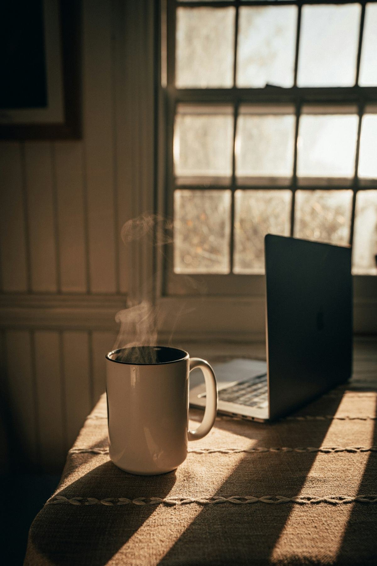 A mug of coffee beside a laptop in morning light
